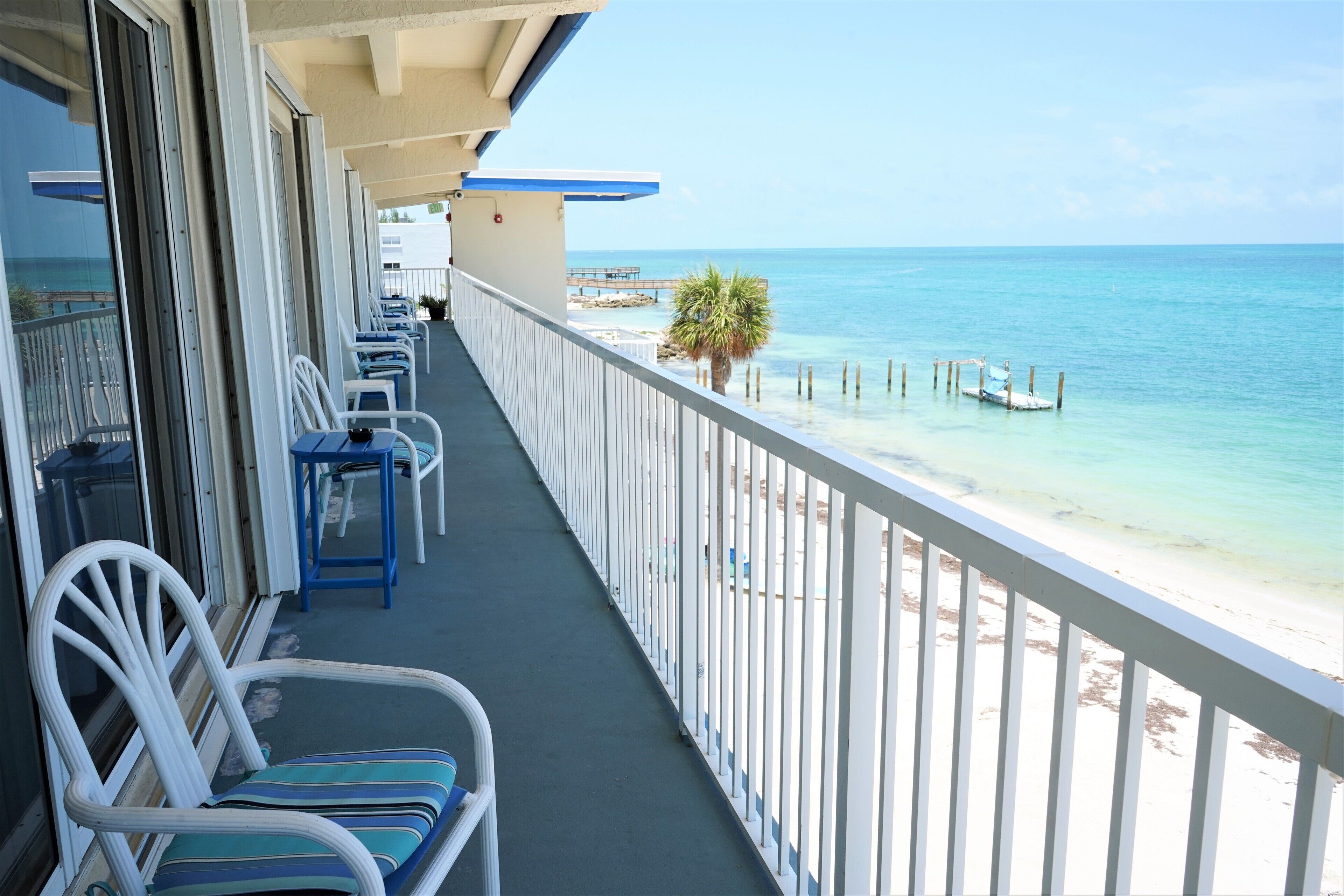 Un balcon avec des balustrades blanches, des chaises bleues et une vue sur la plage et l’océan.