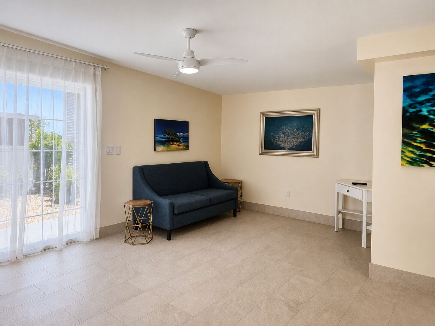 A living room with a sofa, a small table, a ceiling fan, and two framed pictures on the wall.