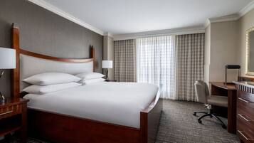 A hotel room with a large bed, a desk, a chair, a dresser, and a mirror.