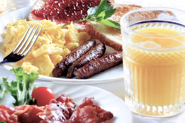 Un plato de desayuno con huevos revueltos, salchichas, tostadas, mermelada, tocino y un vaso de zumo de naranja.