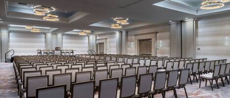 A conference room with rows of chairs, a stage, and modern lighting fixtures.