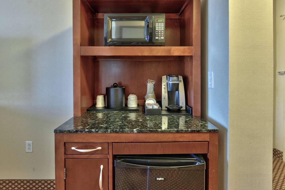 A compact kitchenette with a microwave, coffee maker, and toaster on a granite countertop.