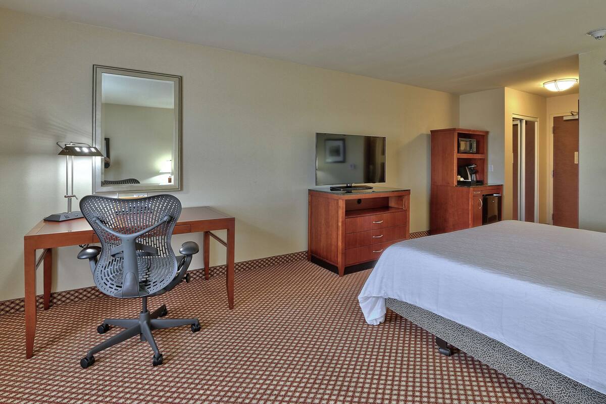 A hotel room with a bed, desk, chair, television, and wardrobe.
