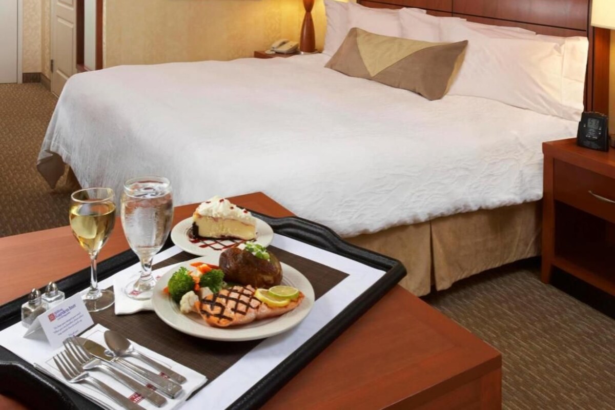 A hotel room with a neatly made bed, a tray with a dessert and drinks, and a bedside table with a lamp.