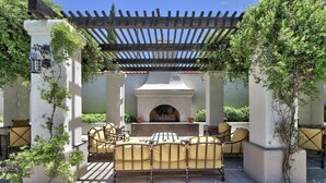 An outdoor patio with a built-in fireplace, surrounded by yellow cushioned chairs and a pergola overhead. - Hilton Garden Inn Las Cruces (Las Cruces)