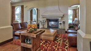 A spacious living room with a fireplace, leather sofas, a wooden coffee table with fruit, and patterned rugs. - Hilton Garden Inn Las Cruces (Las Cruces)