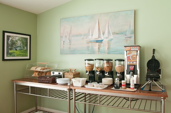 A breakfast bar with coffee machines, a waffle maker, and a painting of sailboats. - Glenmoor By the Sea (Lincolnville)