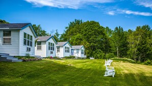 A row of white cabins with a grassy lawn and trees in the background. - Glenmoor By the Sea (Lincolnville)