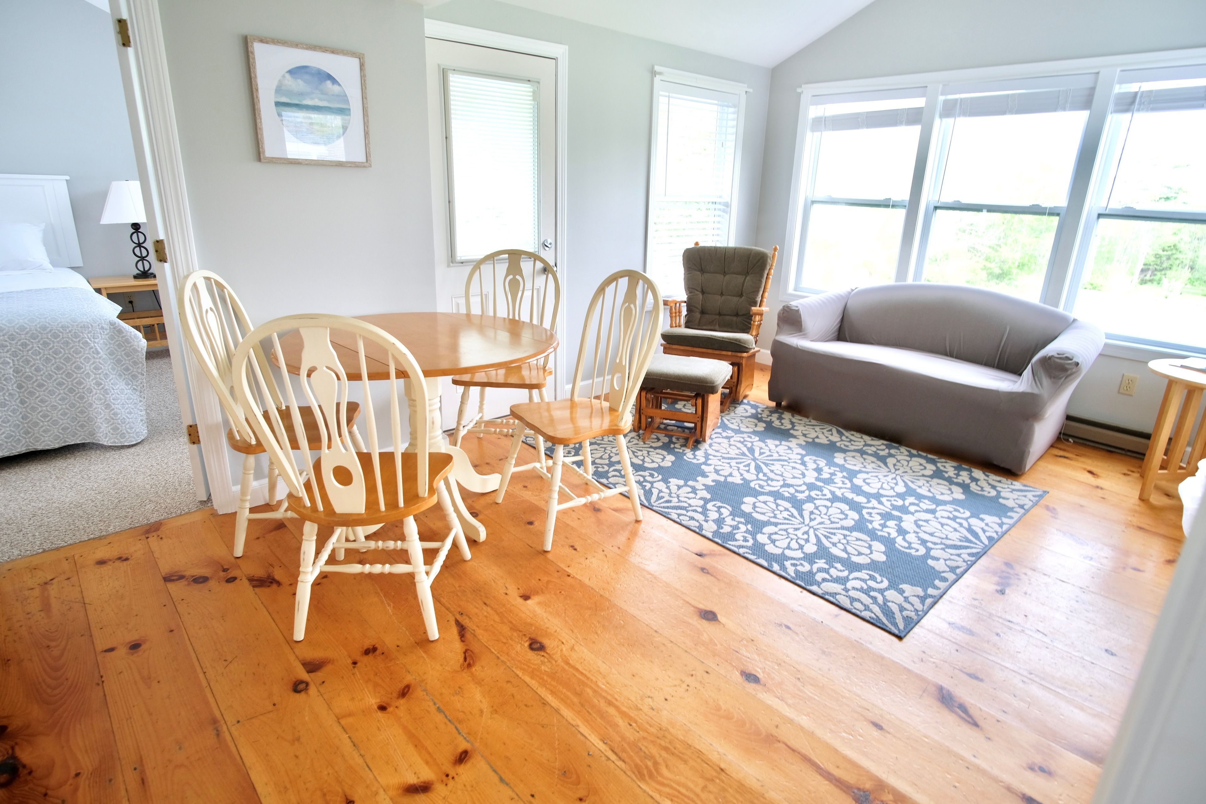 Une pièce comprenant une table à manger en bois, des chaises, un canapé gris et un tapis à motifs.