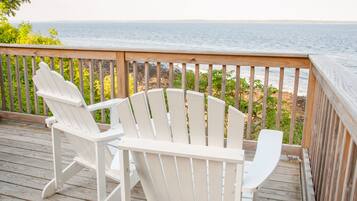A wooden deck with two white Adirondack chairs facing the ocean.