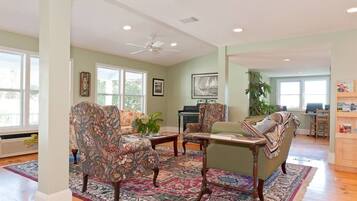 A spacious living room with a large window, a ceiling fan, and a piano.