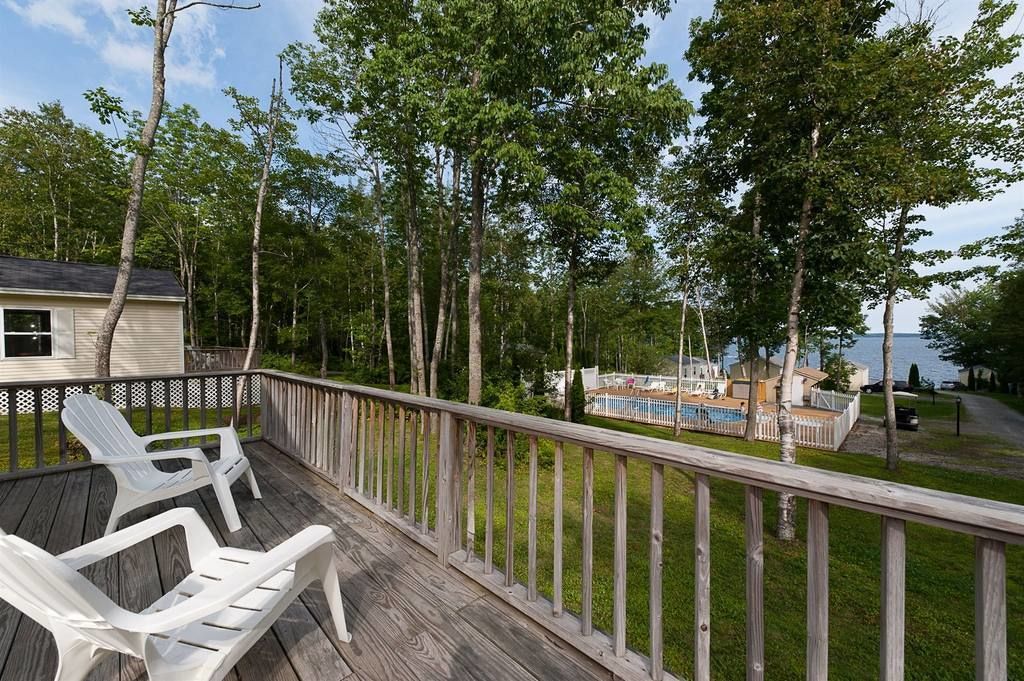A wooden deck with white chairs, a pool, and a view of a lake.