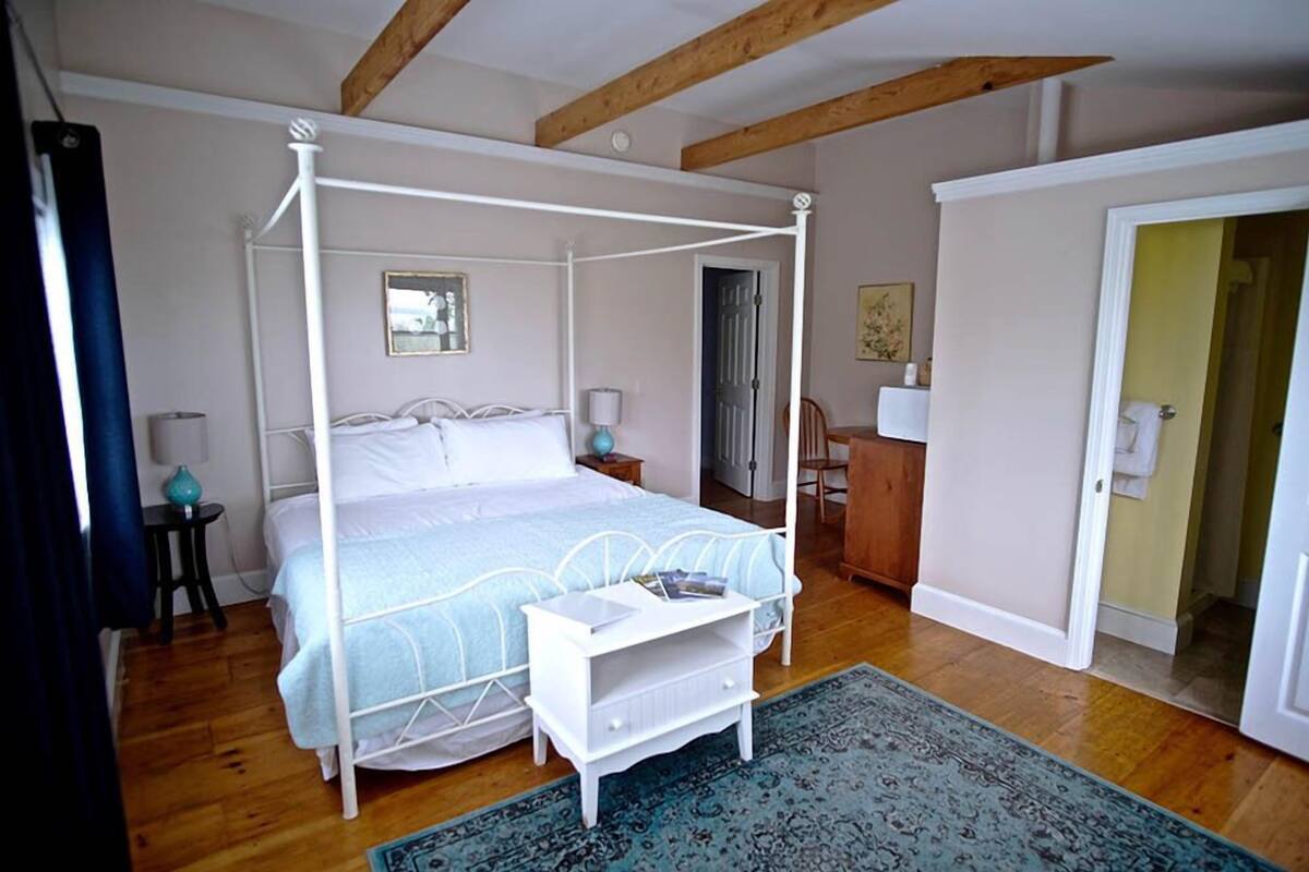 A four-poster bed with a white metal frame, a matching nightstand, and a blue patterned rug.