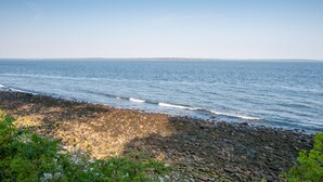 A rocky shoreline with calm sea waves, clear sky, and distant land. - Glenmoor By the Sea (Lincolnville)
