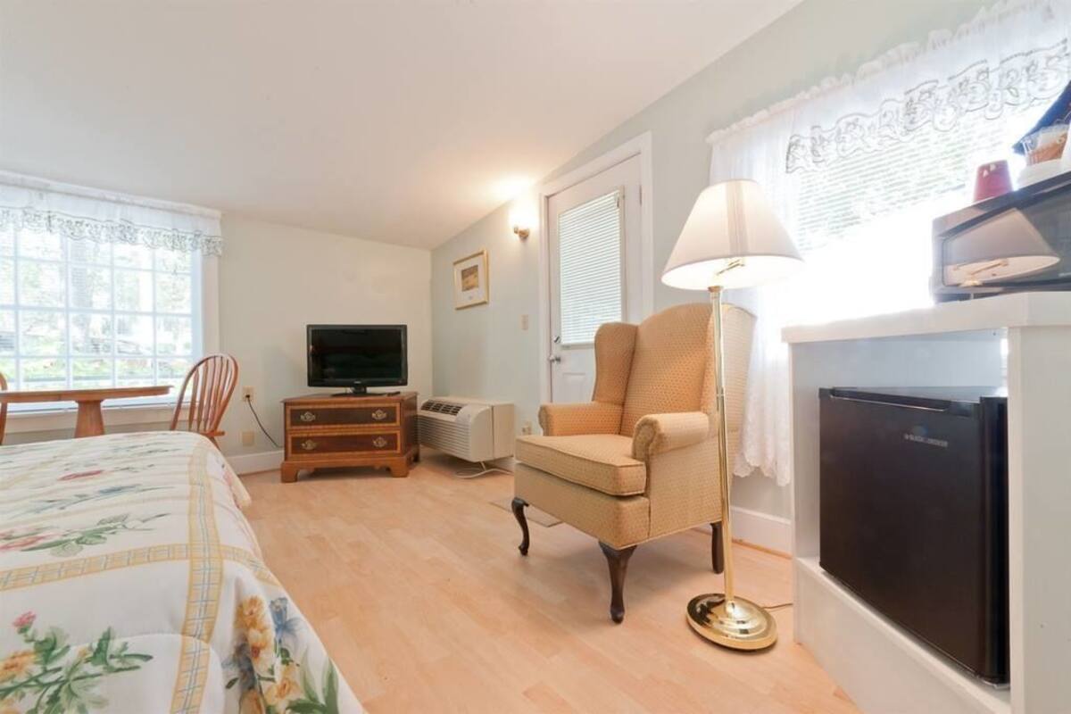 A hotel room with a bed, a TV, a chair, a desk, a lamp, and a refrigerator.
