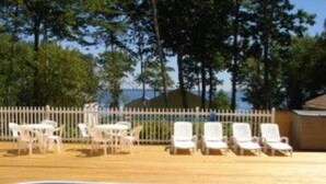 A swimming pool with white lounge chairs and a white fence. - Glenmoor By the Sea (Lincolnville)