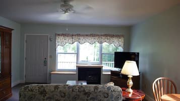 A living room with a sofa, a television, a lamp, a fireplace, and a window with a view of trees.
