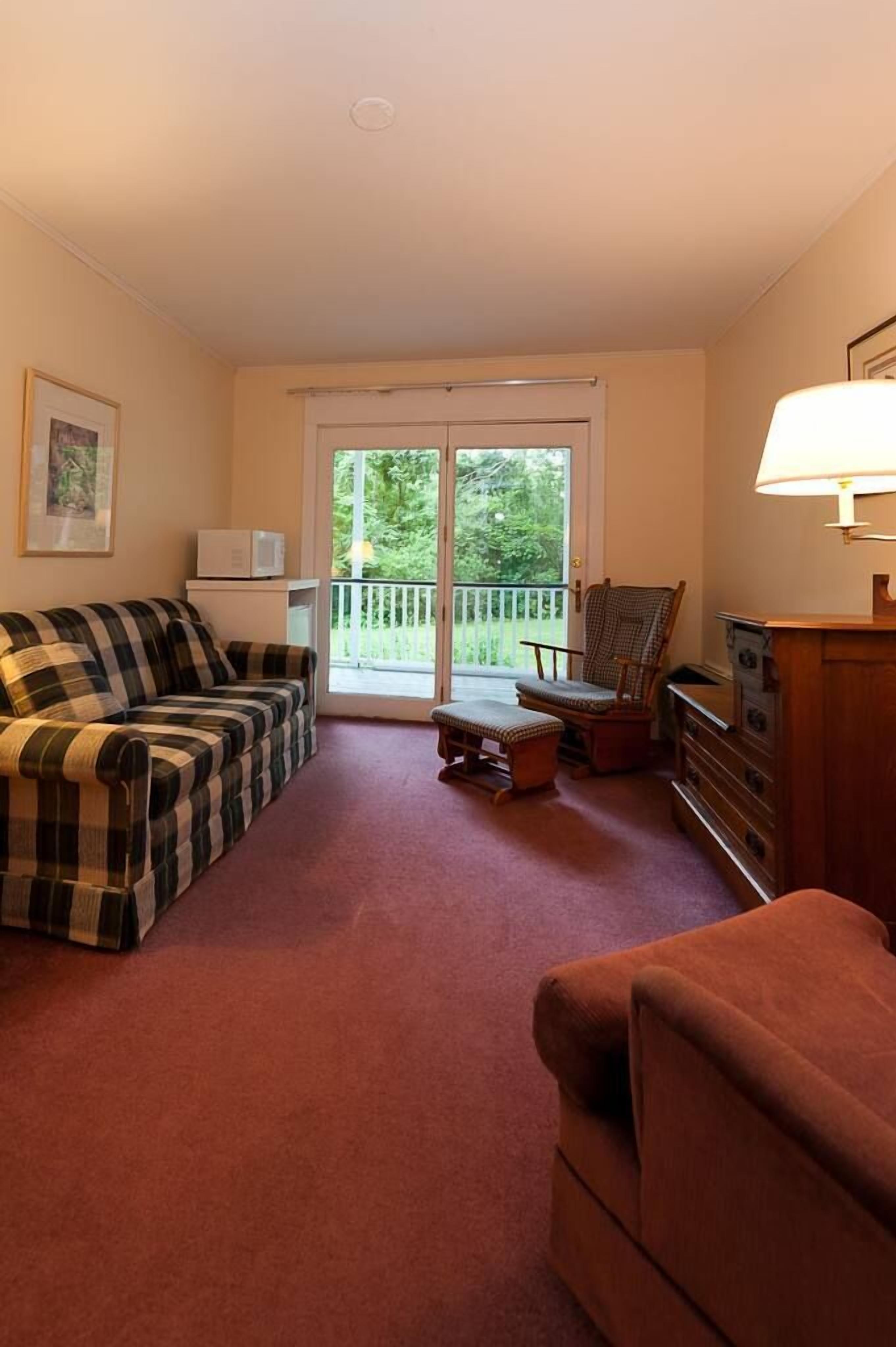 A living room with a plaid sofa, a brown armchair, a wooden cabinet, and a small table.