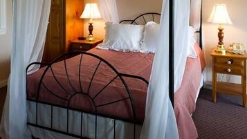 A four-poster bed with white canopies, a ceiling fan, and two bedside lamps.