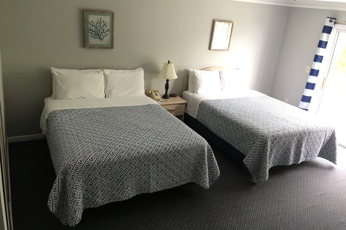 A hotel room with two beds, a nightstand with a lamp, a telephone, and framed artwork on the walls.