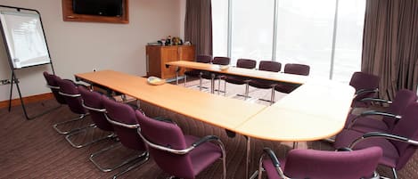 A conference room with a long table, purple chairs, a whiteboard, and a television on the wall.