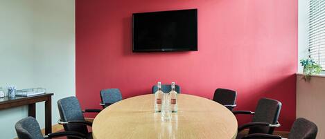 Un salón de conferencias con una mesa redonda, seis sillas, un televisor de pantalla plana en la pared y dos botellas sobre la mesa.