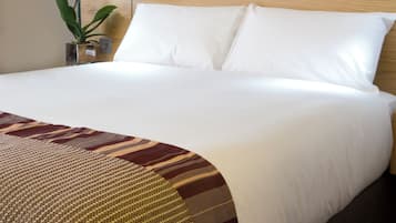A neatly made bed with white linens, a wooden headboard, and a decorative throw blanket.