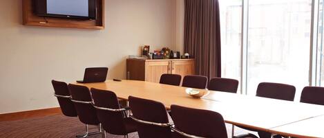 A conference room with a large table, chairs, a television, and a window with curtains.