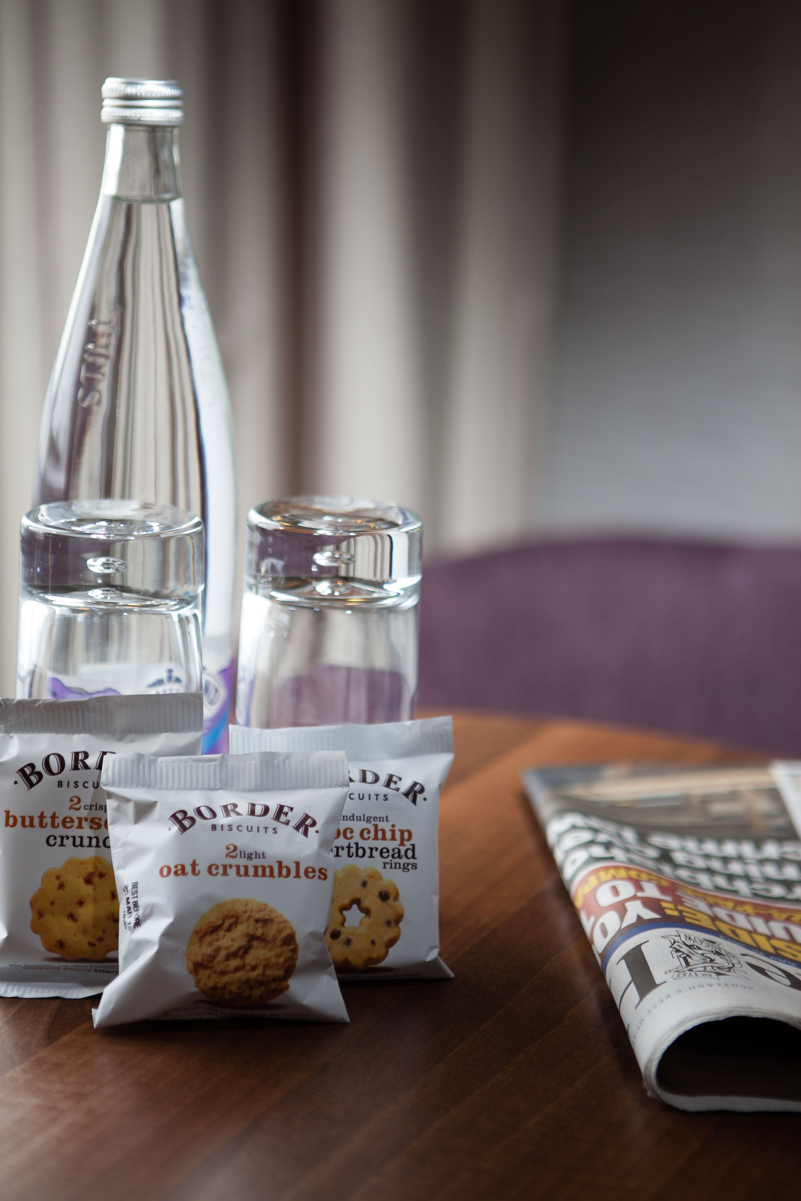 A table with a bottle, salt and pepper shakers, and packets of Border biscuits.