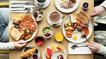 Disposição de café da manhã com diversos pratos, incluindo torradas, ovos, linguiça e um croissant.