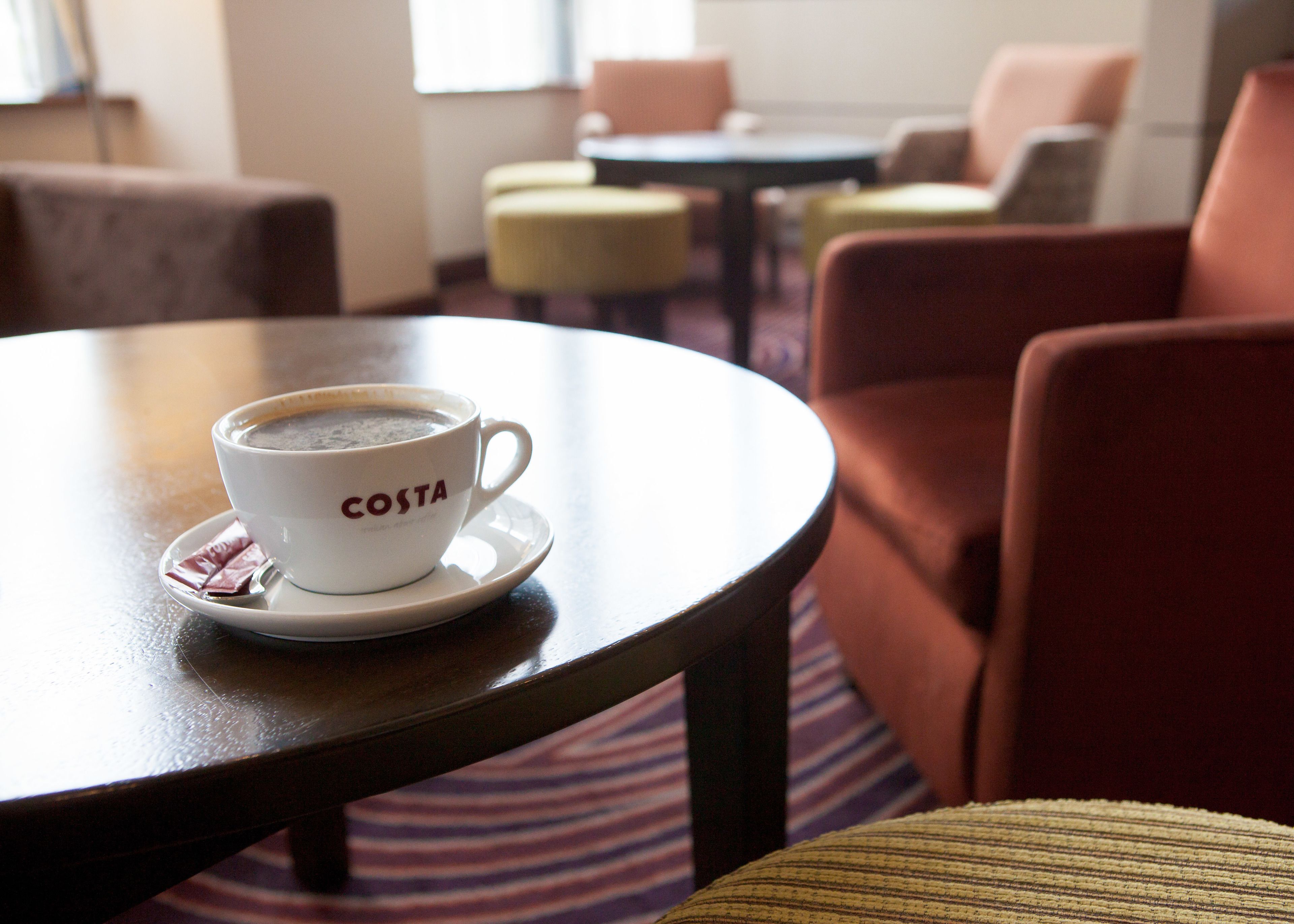 A cup of coffee on a table in a room with chairs and tables.