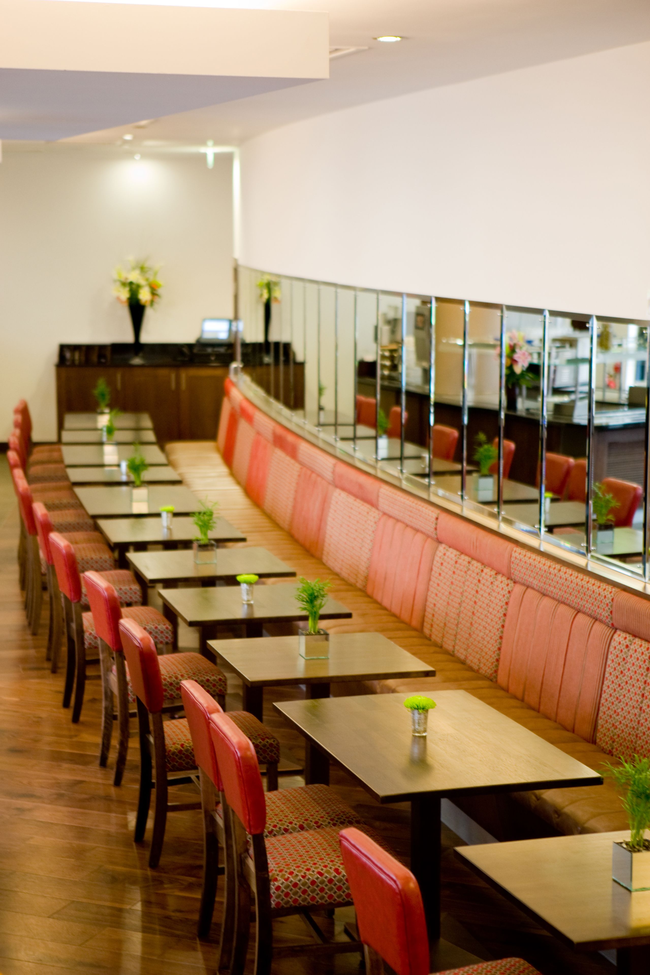 A restaurant with long tables and red cushioned booths, a wooden floor, and a large window with a view of the interior.