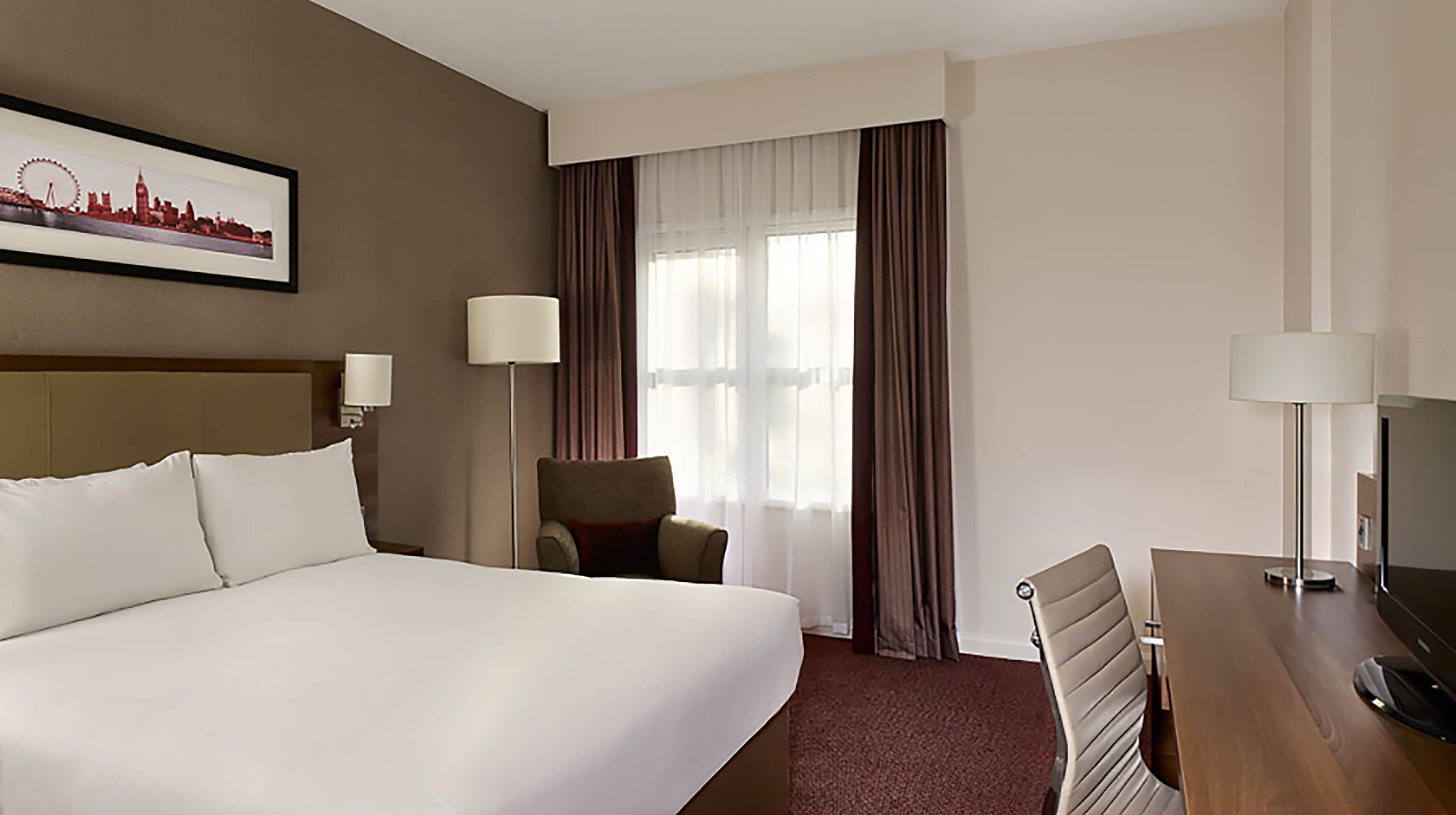 A hotel room with a large bed, a desk, a chair, a television, and a window with curtains.