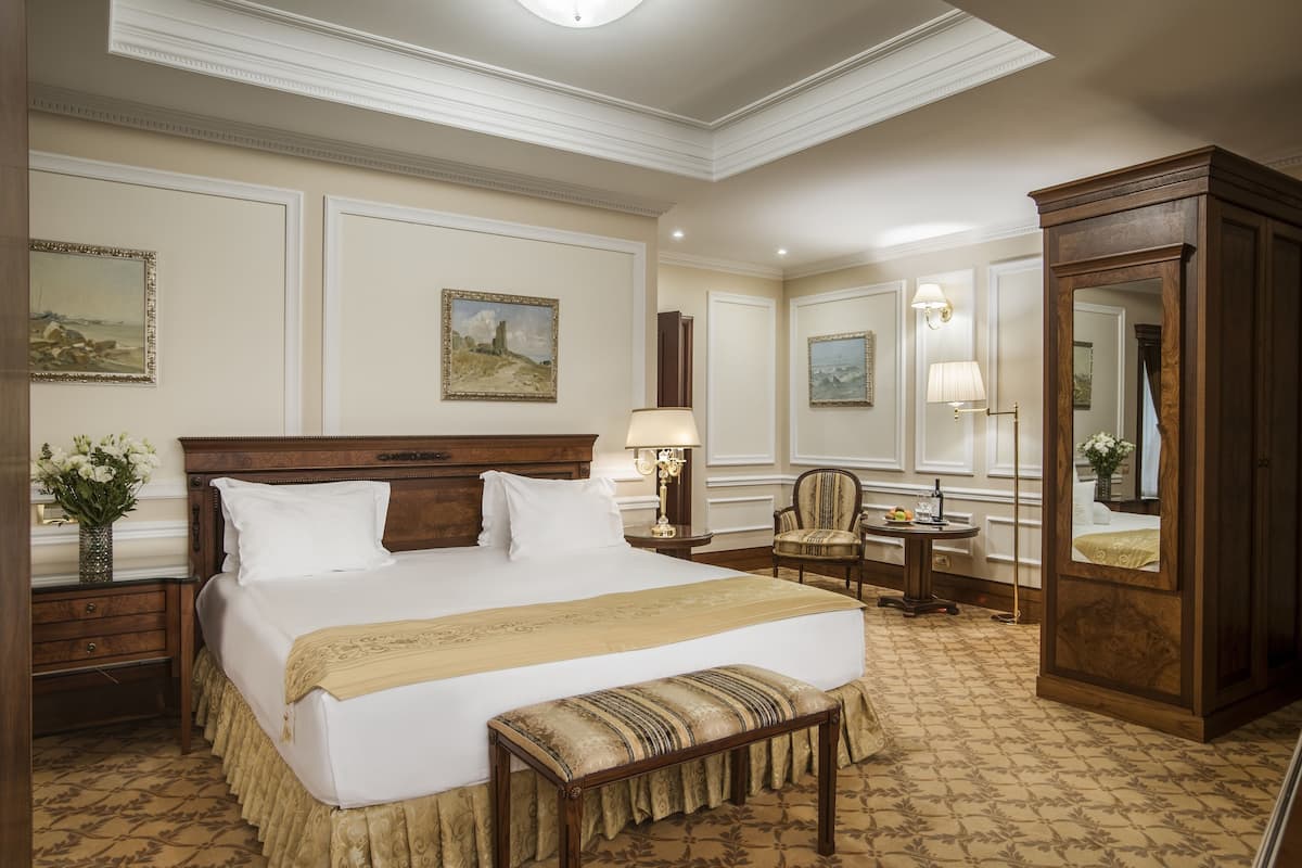 Amplia habitación de hotel con una cama grande, un armario de madera, un escritorio con lámpara y una silla.