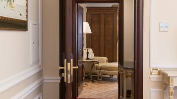 A hotel hallway with a red carpet, a wooden door, a framed picture on the wall, and a small table with a lamp.