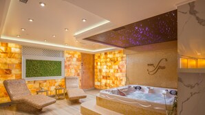 Un cuarto de spa con un jacuzzi, dos sillones de descanso, una pared con mosaico verde y un techo con un despliegue de luces que simulan estrellas.