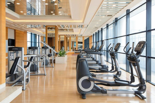 Un gimnasio moderno con cintas de correr, máquinas de pesas y un amplio ventanal que proporciona luz natural.
