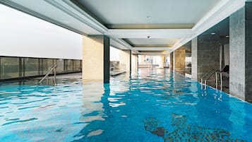 Una piscina interior con agua cristalina, rodeada de pilares de piedra y paredes de vidrio, con vistas al cielo.