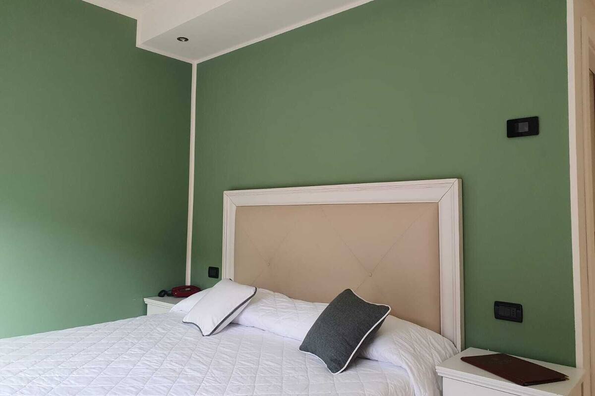 A bedroom with a bed, white bedding, a beige headboard, and green walls.