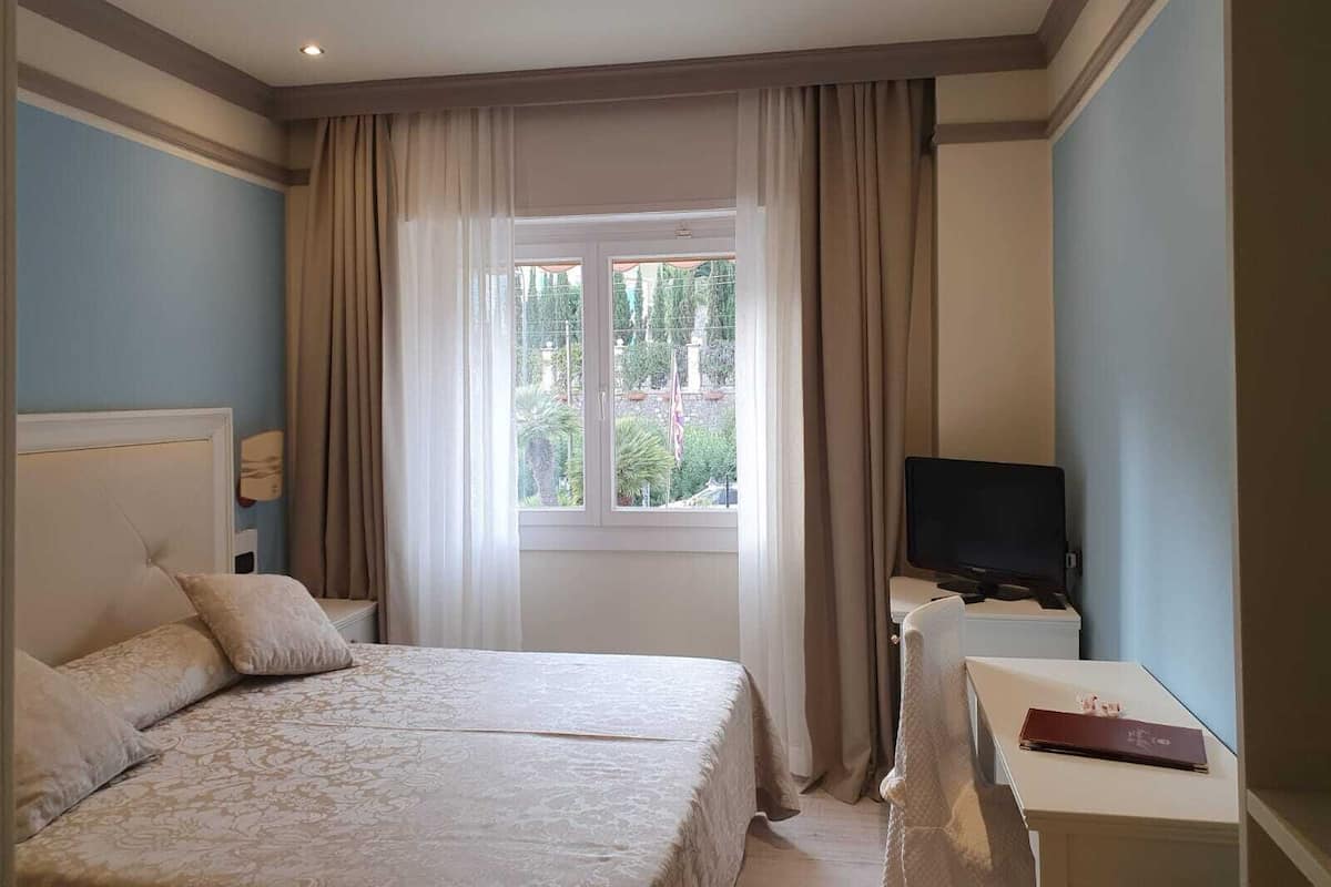 A hotel room with a bed, a desk with a TV, and a window with curtains.
