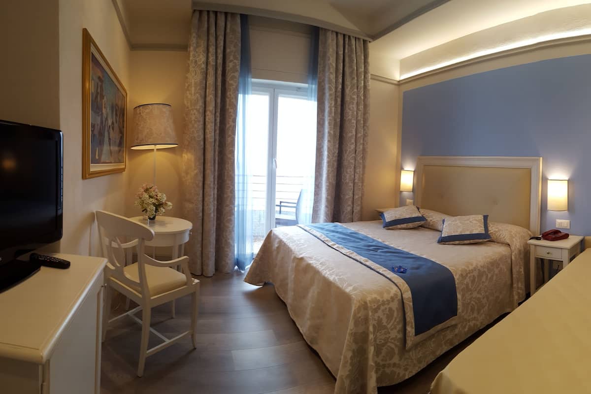A hotel room with a bed, a desk, a chair, a TV, and a window with curtains.