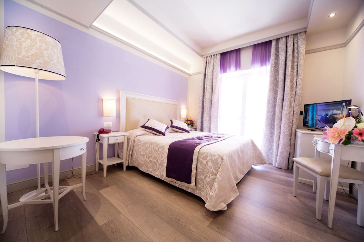 A hotel room with a bed, a desk, a TV, and a lamp.