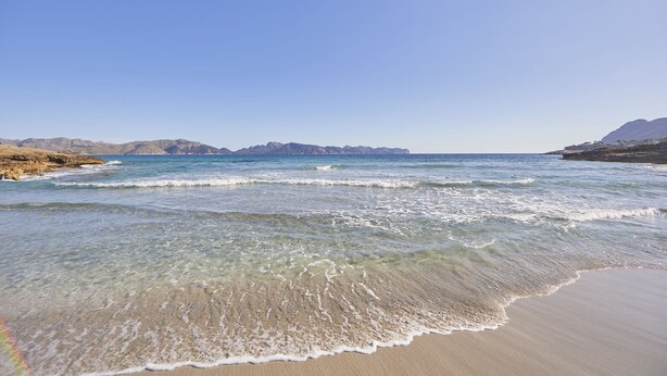 A beach with clear water, sandy shore, and distant mountains. - Prinsotel Mal Pas (Alcúdia)