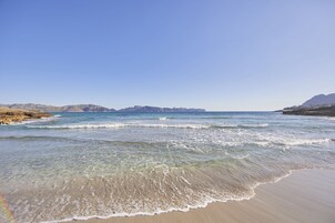 Una playa con agua cristalina, orilla de arena y montañas a lo lejos.