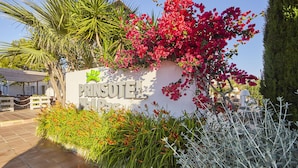 A sign for "PRINSOTEI" with a logo, surrounded by lush greenery and flowering plants. - Prinsotel Mal Pas (Alcúdia)
