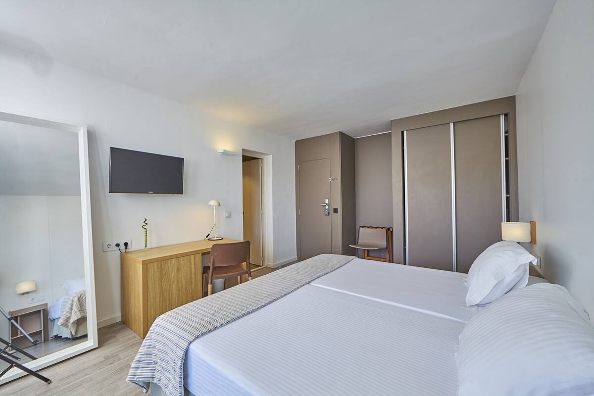 A hotel room with a large bed, a desk, a chair, a television, and a wardrobe.