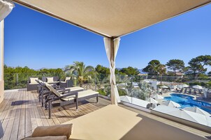 Un balcón con mobiliario de mimbre, una piscina y vistas amplias del paisaje circundante.