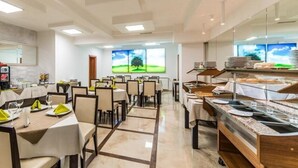 A modern dining area with multiple tables and chairs, a buffet station, and large windows with a view of a green landscape. - Hotel Opal (Cluj-Napoca)