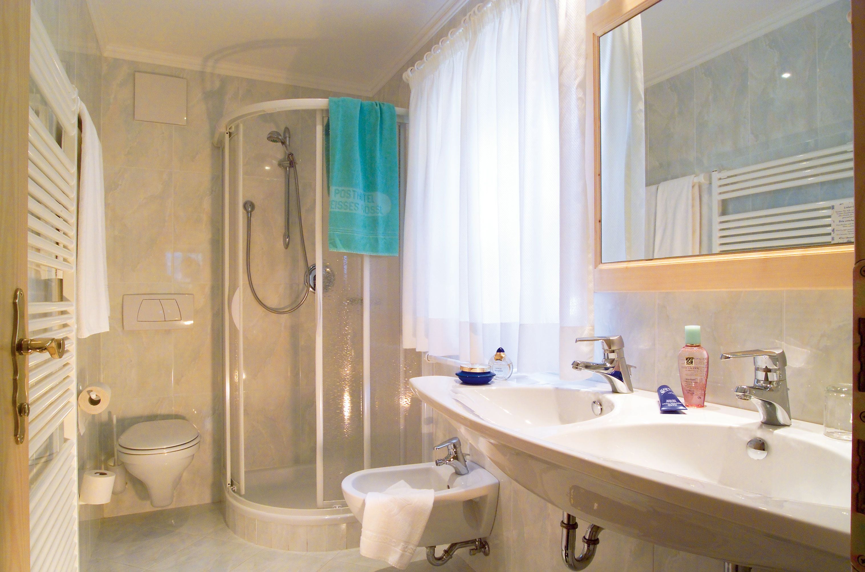 A bathroom with a shower, toilet, bidet, and a sink with a mirror.
