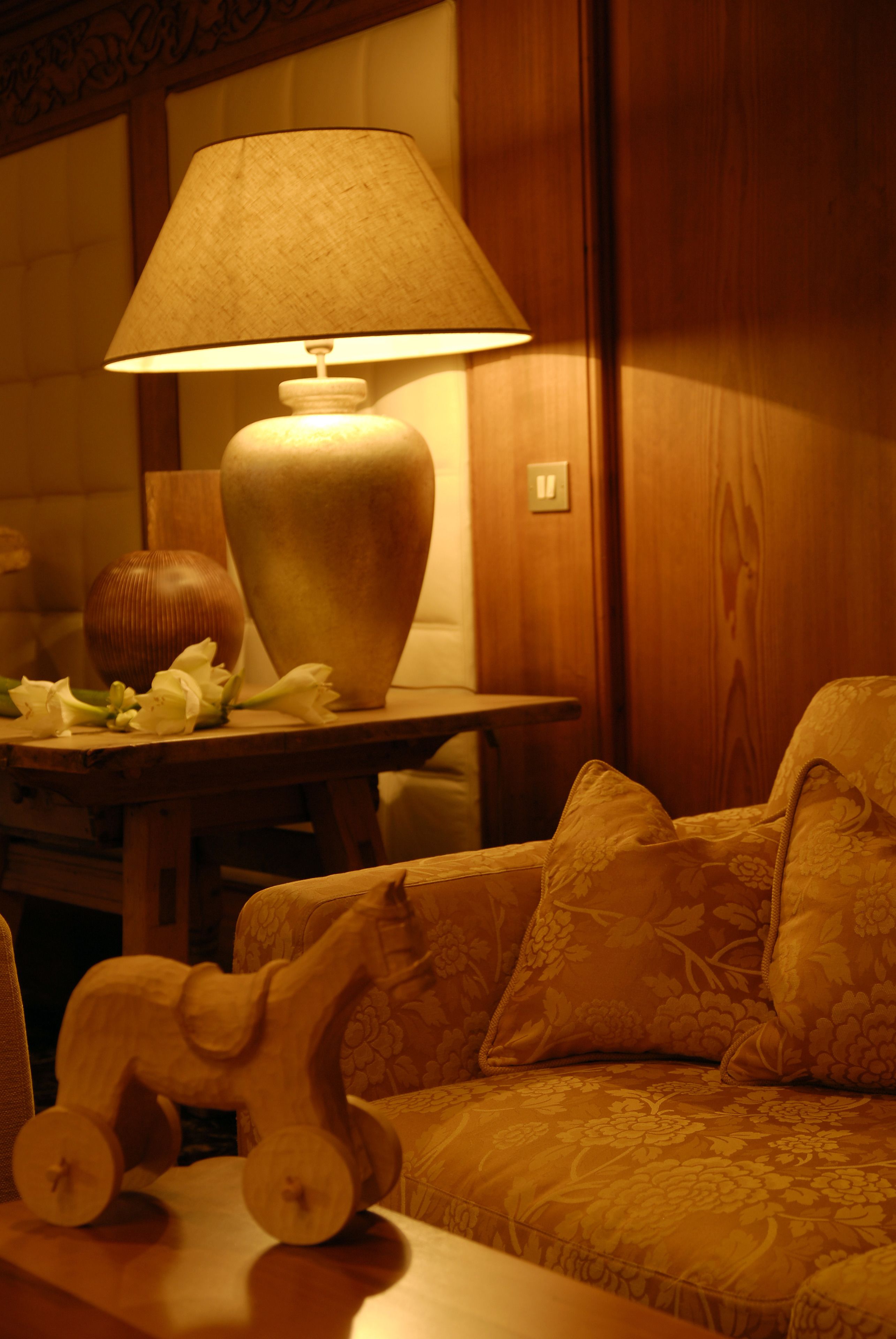 Um quarto com iluminação acolhedora, uma mesa de madeira, um vaso grande e um sofá com padrão floral.